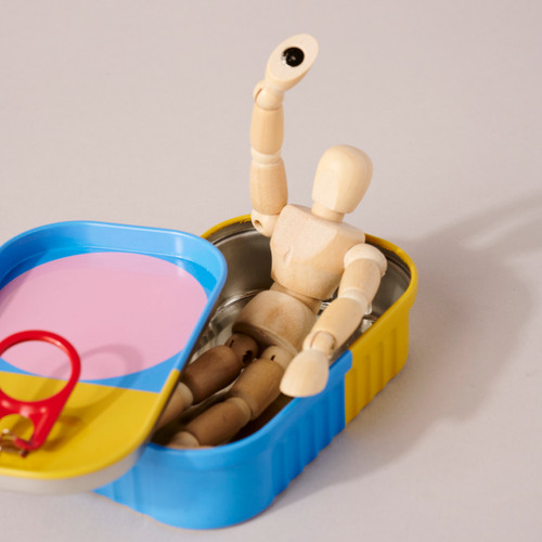 Image of small wood mannequin sitting in colorful tin waiving with tin lid ajar.