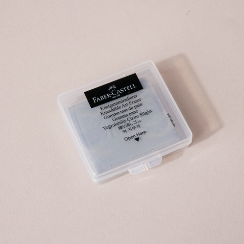 A clear plastic case holding a gray kneadable eraser with Faber-Castell branding and the words kneadable eraser written in several languages.