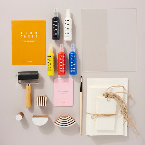Image shows the contents of the Blok Parti Stationery Kit lying flat including paint, wood blocks, paper and a paintbrush.