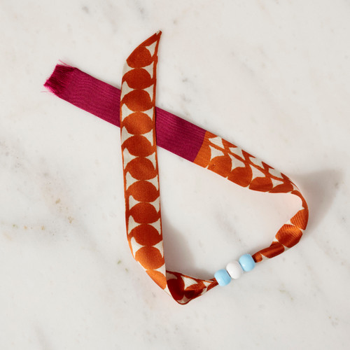 Orange silk ribbon style bracelet with 3 small beads at center of ribbon bracelet