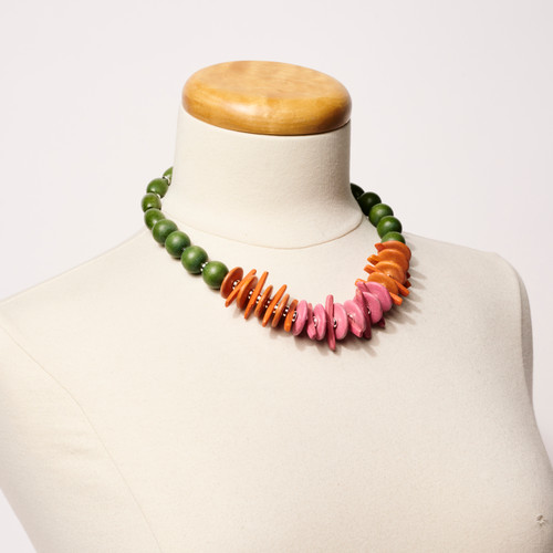 Bold necklace featuring round green beads, flat orange and pink beads at the lower part of the necklace shown on a dress form