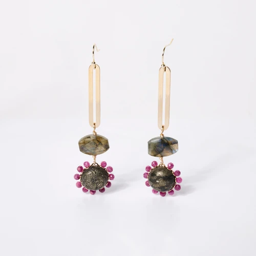 Front view of a pair of dangle earrings made of a gold shaft leading to an earthy gem encircled with red crystals.