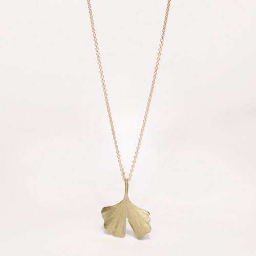Close-up of a gold chain necklace with a gingko leaf pendant.