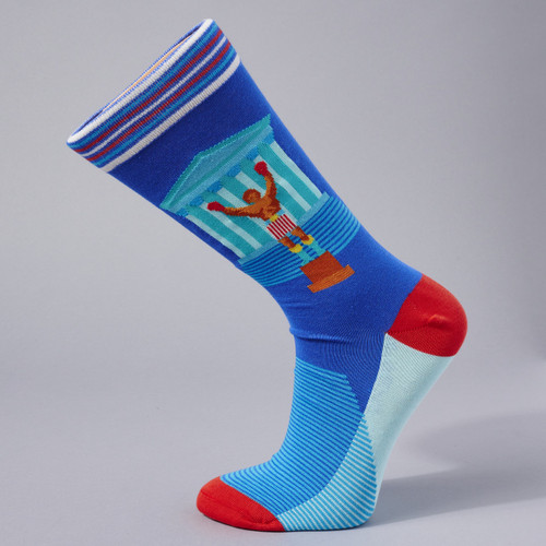 Philadelphia's Champion Socks are shown on a sock form in side view. The champion  boxer stands on a plinth,  with the museum's facade in the background. The socks are primarily blue and red, with stripes at the top and red toes and heels.
