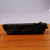 A zippered Blackwing black canvas pencil pouch is shown in a side view sitting upright on a wooden surface. The black leather zipper pull and grip tab are clearly shown.