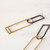 Long earrings featuring rectangular-shaped dark-toned oxidized sterling silver tops interlocking shiny gold-toned brass rectangular shapes laying flat on a surface, showing reverse side of one earring