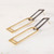 Long earrings featuring rectangular-shaped dark-toned oxidized sterling silver tops interlocking shiny gold-toned brass rectangular shapes laying shown from a side angle