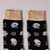Arms and Armor helmet socks depict several styles of armor helmets in silver, interspersed with a beige motif. The body of the socks is black with beige toes and heels. The socks are shown in side view close-up detail and lying flat.