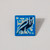 A pin of soft enamel in various shades of blue over base metal depicting a raven is shown on a gray background.