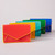 A series of  small envelope style wallets are shown in a line. The wallets are coral, yellow, turquoise, emerald green and cobalt blue in color, each with a contrasted color edging. They are  arranged standing on a grey surface.