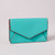 A turquoise envelope wallet with brown contrast edging stands closed on a grey surface.
