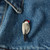 Grey, white, and black painted porcelain bird pin attached to denim jacket