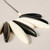 Detail of necklace of oblong alternating black and cream beads arranged in a semi-circle and strung on black cording shown laying flat