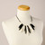 Necklace of oblong alternating black and cream beads arranged in a semi-circle and strung on black cording shown on dress form