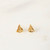 A frontal close-up of a small pair of gold sailboat stud earrings.