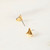 A frontal close-up of a small pair of gold sailboat stud earrings with one of the earrings flipped to show the stud post.