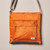Detail image front of orange nylon crossbody bag, small ORI label sewn on lower right corner