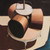 A close up of a poster depicting a painting of three short brown cylinders arranged on a table with a mechanical device hovering over them. The image roughly resembles a brown drum kit on a stage under a spotlight.