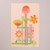 This poster depicts several blooming flowers in abstract form. The background color of the poster is a pale peach color. The flowers are varying shades of oranges, pinks, greens and blues. This view shows the full poster.