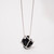 Detail of a pendant necklace featuring a hollow silver-toned cube encasing black rubber form suspended by smooth silver-toned chain