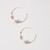 Pair of thin gold-tone wire hoop earrings with small transparent 3 grey glass beads and 3 small gold-tone beads on each shown laying flat