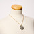 Round sparkly pendant consisting of tiny 'pedals' covered in glitter-like dust on twisted gold-tone chain shown hanging on dress form