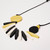 Detail of necklace with round coin-shaped yellow and black beads with multiple oblong beads of black, yellow and white in between strung on black cord shown laying flat