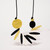 Detail of necklace with round coin-shaped yellow and black beads with multiple oblong beads of black, yellow and white in between strung on black cord