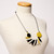 Necklace with round coin-shaped yellow and black beads with multiple oblong beads of black, yellow and white in between strung on black cord and draped on dress form falling at chest level