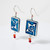 Pair of square blue embossed ceramic earrings with small beads suspended beneath shown at an angle