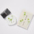 A white ceramic dish with a green floral design sits next to a cream packet with the same design.
