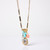 Front view of a gold chain link necklace with a pendant cluster of porcelain, turquoise, and shell gems.
