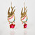 Close-up of a pair of gold dangle earrings in the shape of songbirds in flight with pink and green glass beads and a red glass rose.