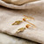 Close-up view of a pair of fern leaf dangly earrings laid flat on their front to show the earring hooks.