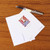 The back side of a notecard showing a small image of a painting of a black horse above a blue aquatic field with floral motifs around is shown next to an envelope and fountain pen.