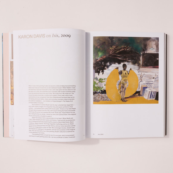 "Noah Davis" opened, showing a block of text titled "Karon Davis on Isis, 2009" on the left page and the Isis painting on the right page. The Isis painting is of a black woman standing in front of a simple house wearing a yellow leotard and matching skirt, the hem of which she is holding by her shoulders creating a halo-like effect around her silhouette.