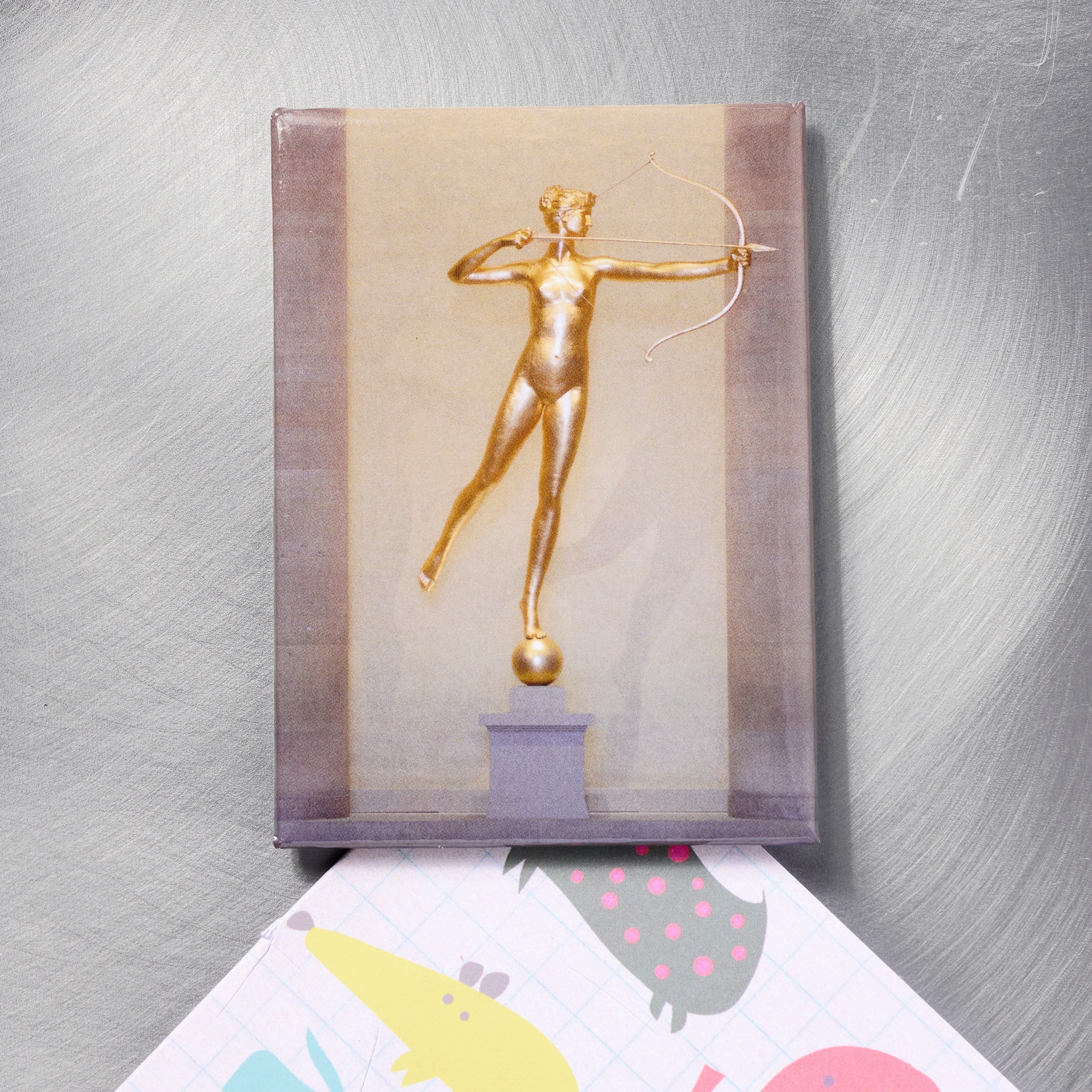 Magnet featuring a golden statue of an archer on a metallic surface.