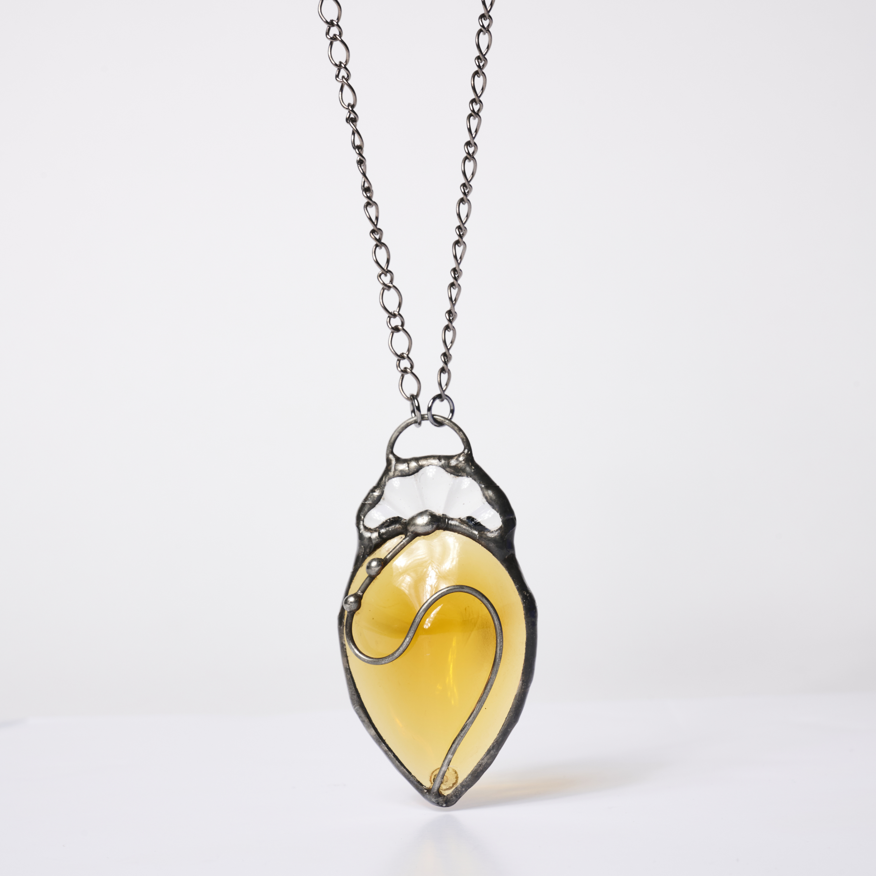 A yellow glass pendant in a metal frame on a chain necklace.