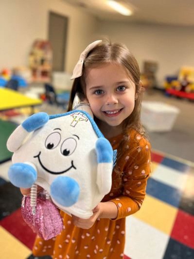 The girl's joyful expression and the vibrant setting emphasize the playful and comforting nature of the toy. Playsets and coloring sheets are sold separately.