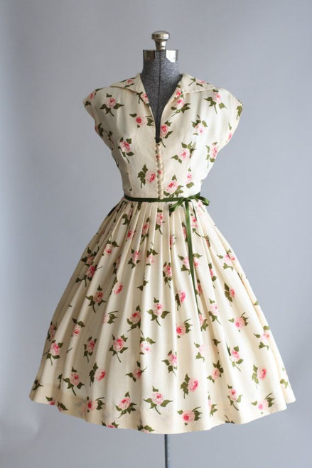 Off white dress with pink floral design and green belt.