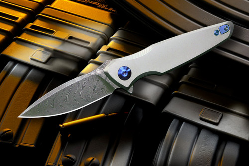 Presentation-side view of the Spartan Blades Pandia folding knife with 6AL4V titanium frame, blue anodized titanium hardware, spear-point Chad Nichols Damascus blade, flipper tab, and clean minimalist handle profile.