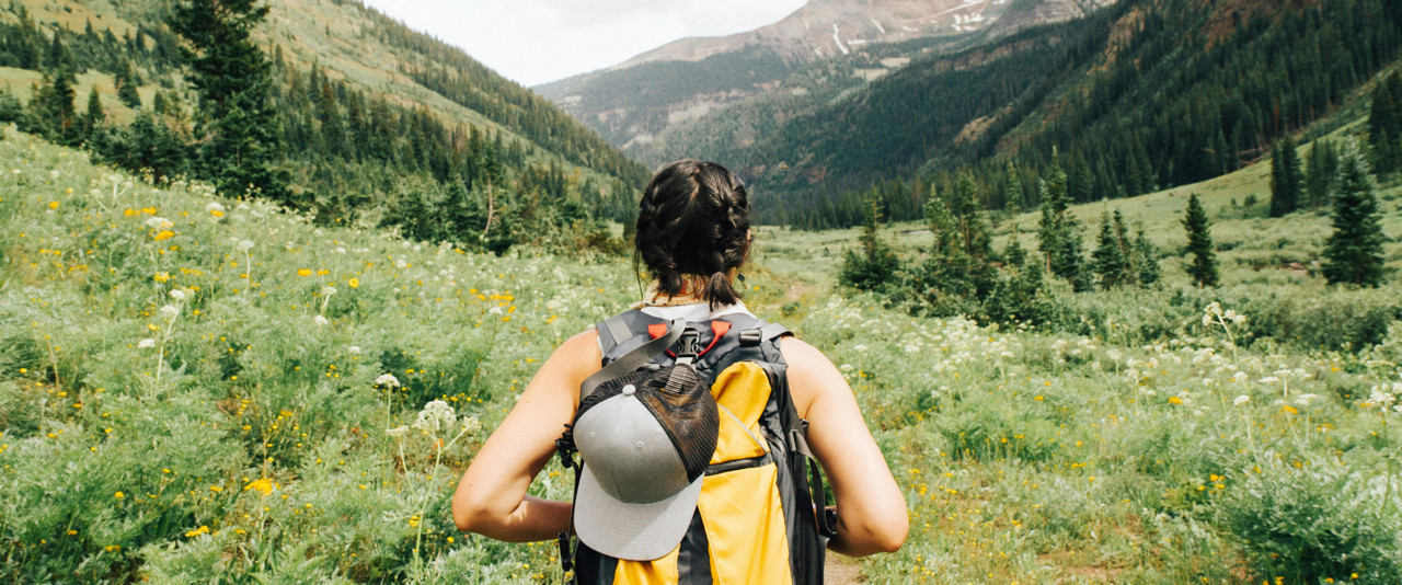 Girl With Yellow Backpack & Grey Hat Hiking In Meadow