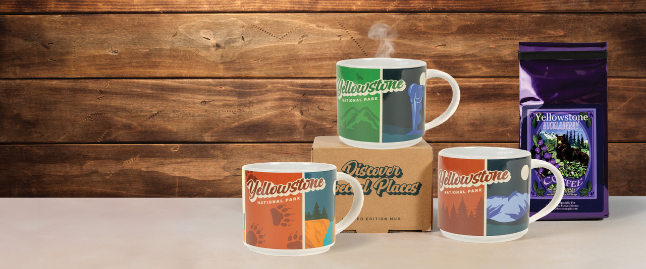 Various Yellowstone mugs with steam coming out of them sitting beside a bag of huckleberry coffee on a countertop.
