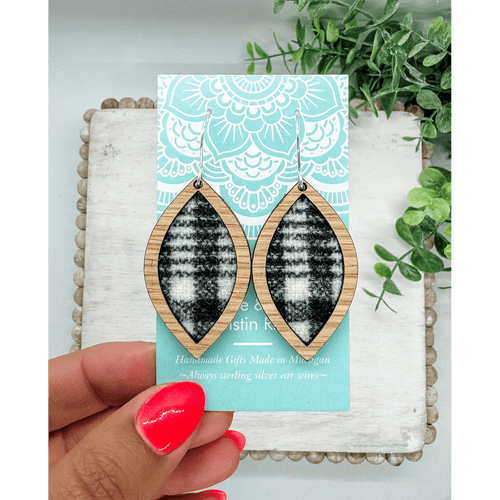 Pair of leaf shaped earrings made of a light wood framing black and white wool fabric