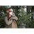 Image of a man leaning on a traditional wooden snowshoe in front of evergreen trees. He is wearing a red/black plaid Trapper Hat and and olive green quarter zip.