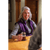 Photo of a woman sitting at a bar holding a beer and smiling. She has shoulder-length silver hair and is wearing a gray shirt with a Plum Passion Ida Outfitter Vest. Photo of a woman sitting at a bar holding a beer and smiling. She has shoulder-length silver hair and is wearing a gray shirt with a Plum Passion Ida Outfitter Vest.