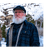 Older man with white beard staning outside in the winter at the base of a mountain.