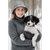 Front image of a woman standing outside in the winter holding a black and white puppy. The woman is smiling and wearing a black and white Iron Belle hat and a gray shirt.