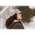 Photo of a woman with long dark hair standing outside in winter and looking to the side. She is wearing a fawn plaid Sidekick Cap and a brown plaid hooded jacket.