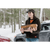 A young woman carrying firewood in the winter with a car in the background. She is wearing the Stormy Kromer Lighthouse Jacket in evergreen plaid.